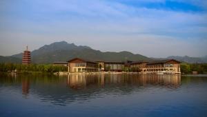 un edificio en un lago con montañas en el fondo en Yanqi Hotel, Managed by Kempinski en Huairou