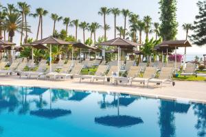 una piscina con sillas, sombrillas y palmeras en Cavo Maris Beach Hotel en Protaras