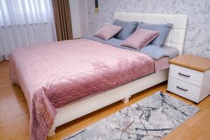 ein Bett mit rosa und blauer Bettwäsche und einem Tisch in der Unterkunft Apartman Mona in Teslić