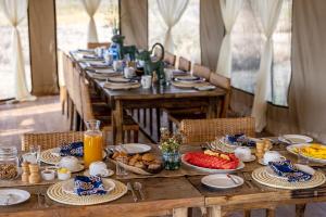 una larga mesa de madera con platos de comida. en Olmara Camp, en Serengeti