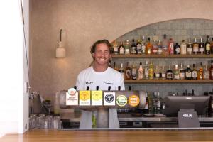 un homme debout derrière un bar avec une boîte d'alcool dans l'établissement Wake Up! Byron Bay, à Byron Bay