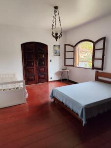 1 dormitorio con cama, ventana y lámpara de araña en Casa Aconchegante - Circuito Teresópolis Friburgo en Teresópolis