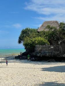 een groep mensen op een strand met een hut bij Lekker Lodge & Restaurant in Jambiani