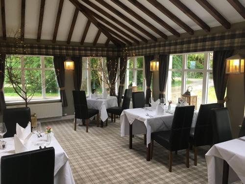 un comedor con mesas y sillas blancas y ventanas en Greshornish House Hotel en Edinbain