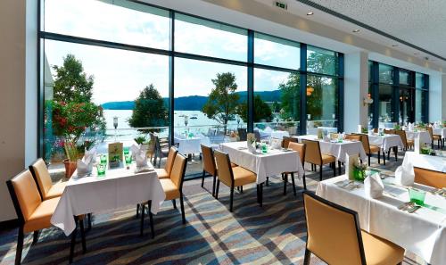 a restaurant with white tables and chairs and large windows at Parkhotel Pörtschach - Das Hotelresort mit Insellage am Wörthersee in Pörtschach am Wörthersee