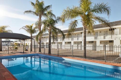 uma piscina com palmeiras em frente a um edifício em ibis Styles Tamworth em Tamworth