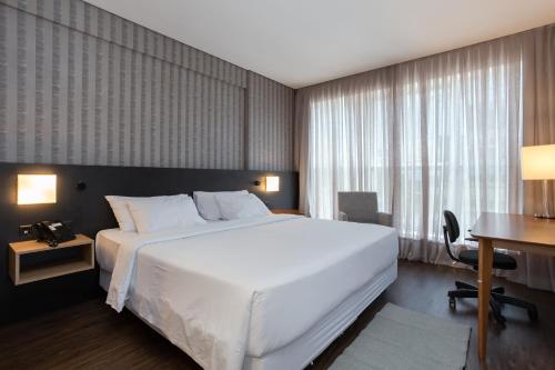 1 dormitorio con 1 cama blanca grande y escritorio en Hilton Garden Inn Praia Brava en Itajaí