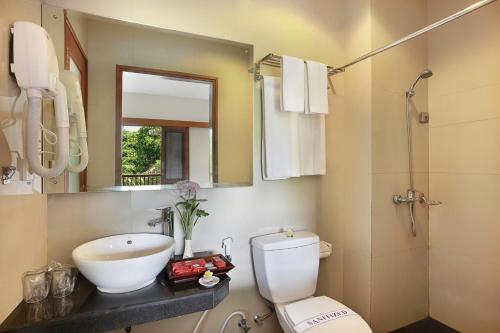 La salle de bains est pourvue d'un lavabo, de toilettes et d'un miroir. dans l'établissement Respati Beach Hotel, à anur