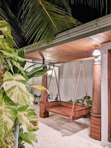 a wooden swing hanging from a porch with plants at Araam Inn in Nellaidhoo