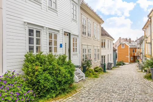 Homerentals Apartments - Behind Bryggen & historic cobblestone streets في بيرغِن: شارع مرصوف بالحصى به بيوت بيضاء وزهور