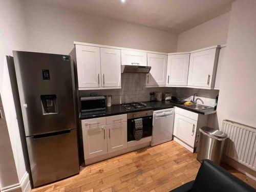 cocina con armarios blancos y nevera de acero inoxidable en 2 bed garden flat West Dulwich FREE STREET PARKING en Londres