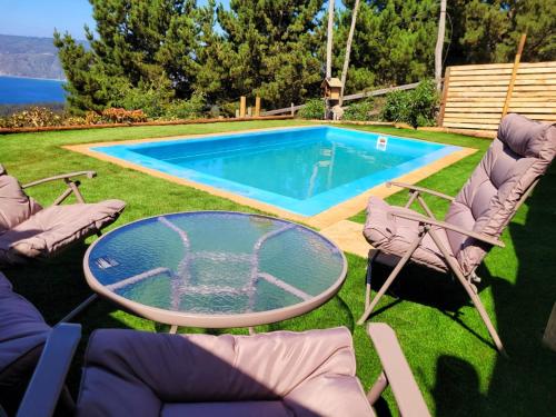 una piscina con sillas y una mesa de cristal en el patio en Cabaña Punta Del Cerro, con Piscina, Tinaja caliente y vista al Mar en Valparaíso