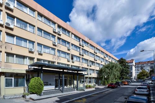 un gran edificio en una calle de la ciudad con coches aparcados en Hotel Sumadija en Belgrado