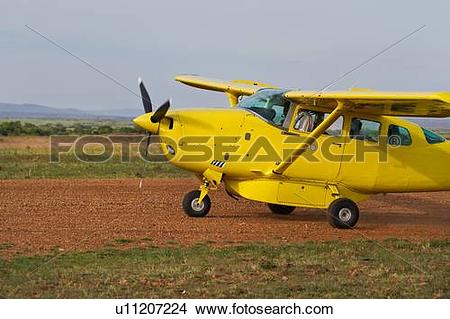 Stock Photo of Side view of yellow Cessna plane on dirt runway.