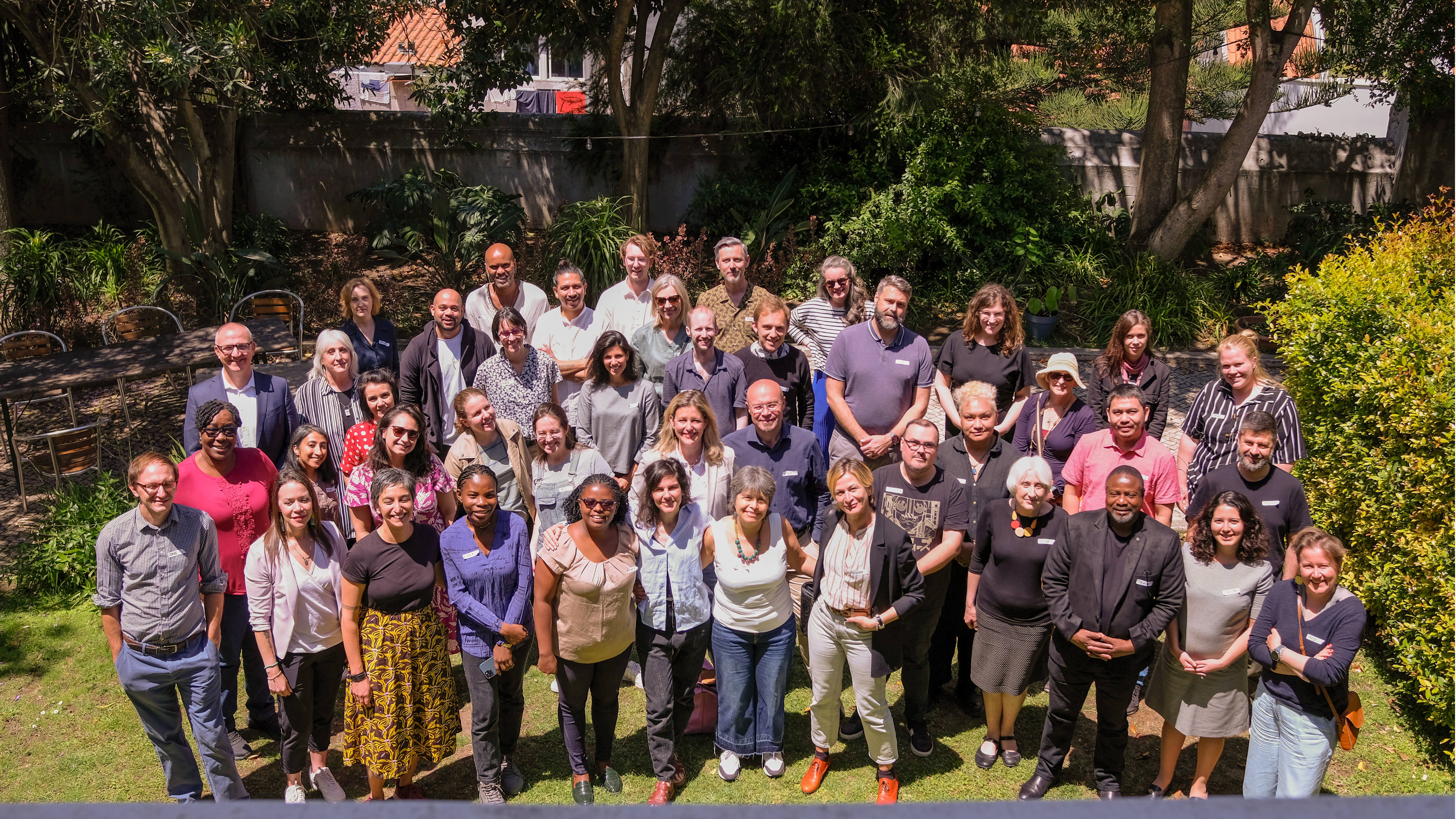 A group of people standing together looking at the camera in a green garden.