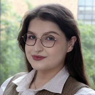 Evan is shown in a head-and-shoulders portrait. She has long brown hair and wears brown glasses and a white shirt.