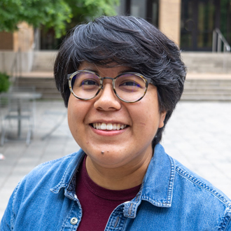 Laura is facing forward and smiling. She has short dark hair and wears a blue denim shirt.