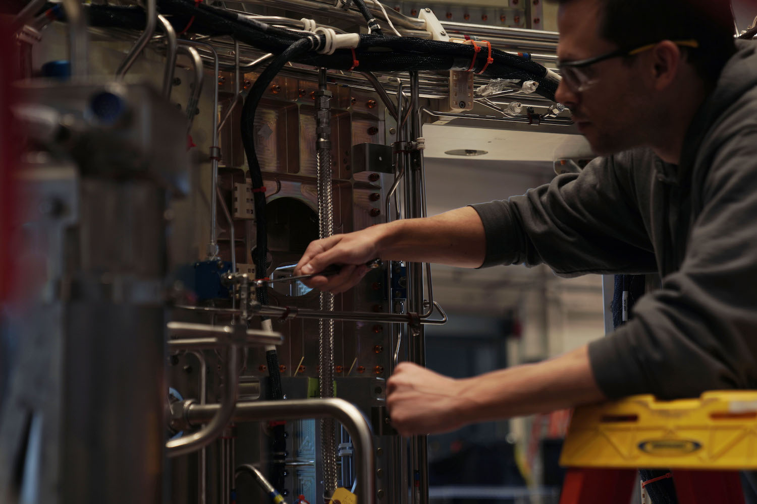 A Blue Origin employee wearing safety glasses and a gray sweatshirt adjusts machinery.