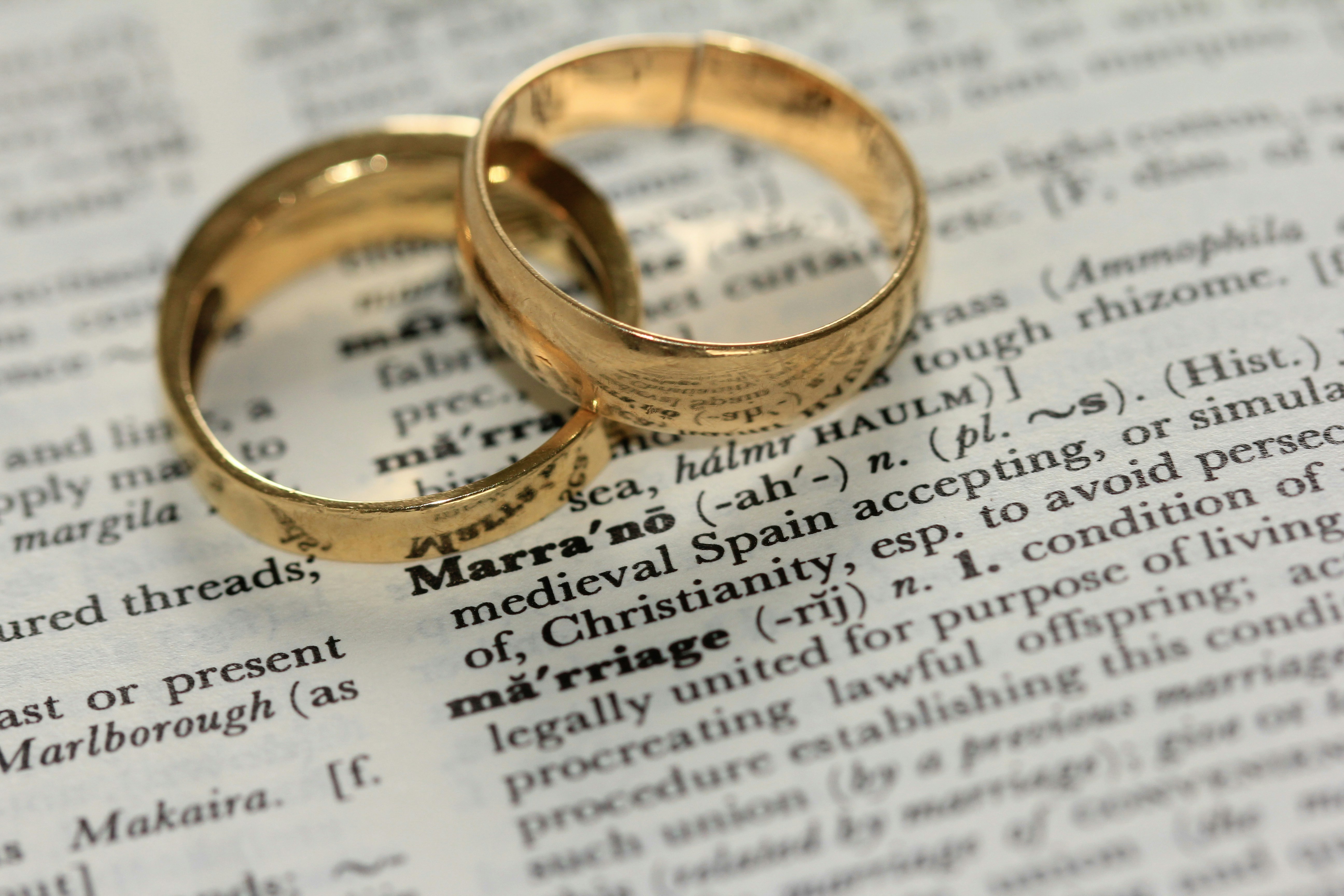 two gold wedding rings laying n top of a dictionary page above the definition of the word "Marriage" 