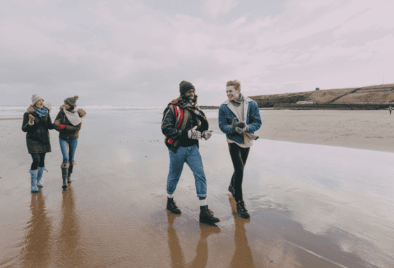 four friends walking and talking along the beach during winter