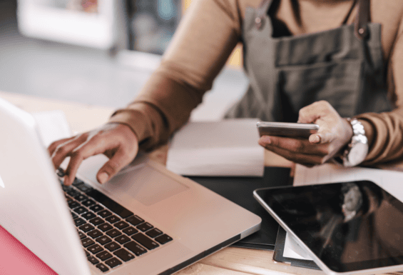 person holding phone and typing on laptop