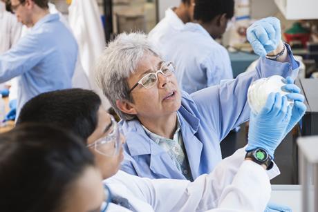 Chemistry pupil in laboratory holds up experiment while teacher points something out