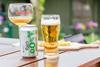 A can of Carlsberg 0.0% alcohol-free beer and a glass sitting on a picnic table outdoors with some snacks on a sunny day