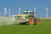 A tractor spreading fertilizer pellets on a field with wind turbines in the distance