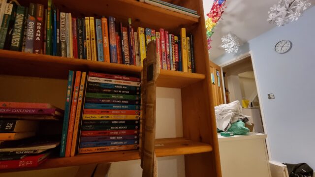 The same bookshelf, but now with the older books - actually fake fronts - swung open to reveal an empty cabinet behind.