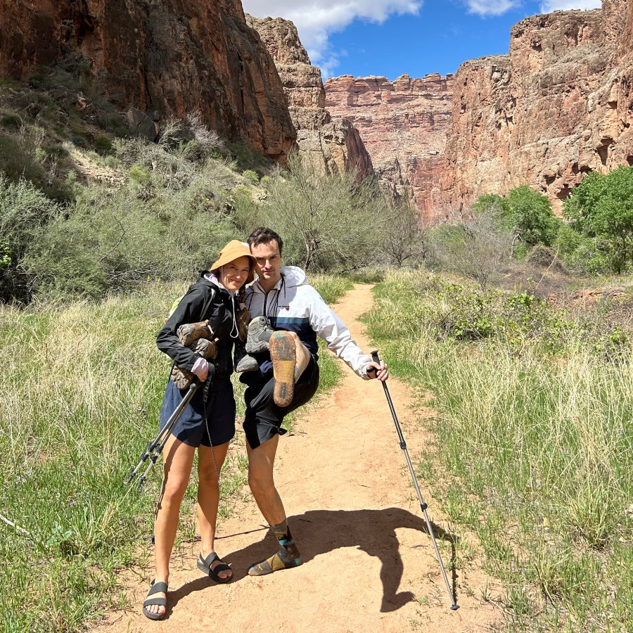 Delfina and her partner on the trail, holding up a sock-clad foot from hiking just in socks