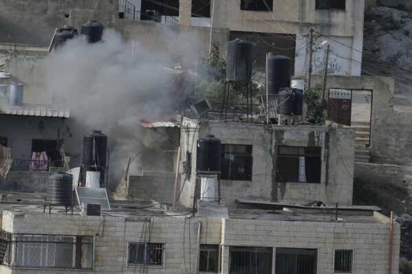 EDS NOTE: GRAPHIC CONTENT - An explosion is seen as three bodies lie motionless on rooftops in the West Bank town of Qabatiya during a raid, Thursday, Sept. 19, 2024. (AP Photo/Majdi Mohammed)