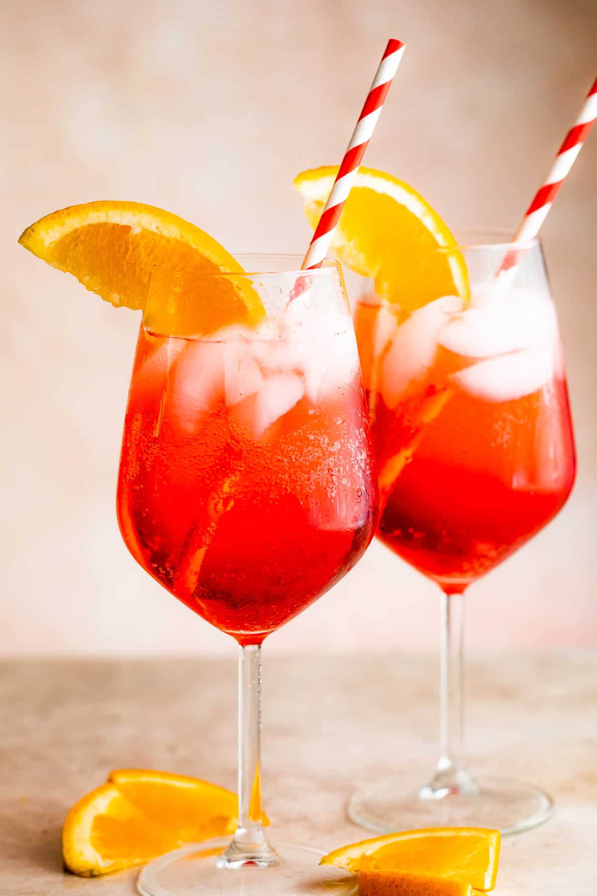 Two tall stemmed glasses with Campari Spritz served with a red and white straw