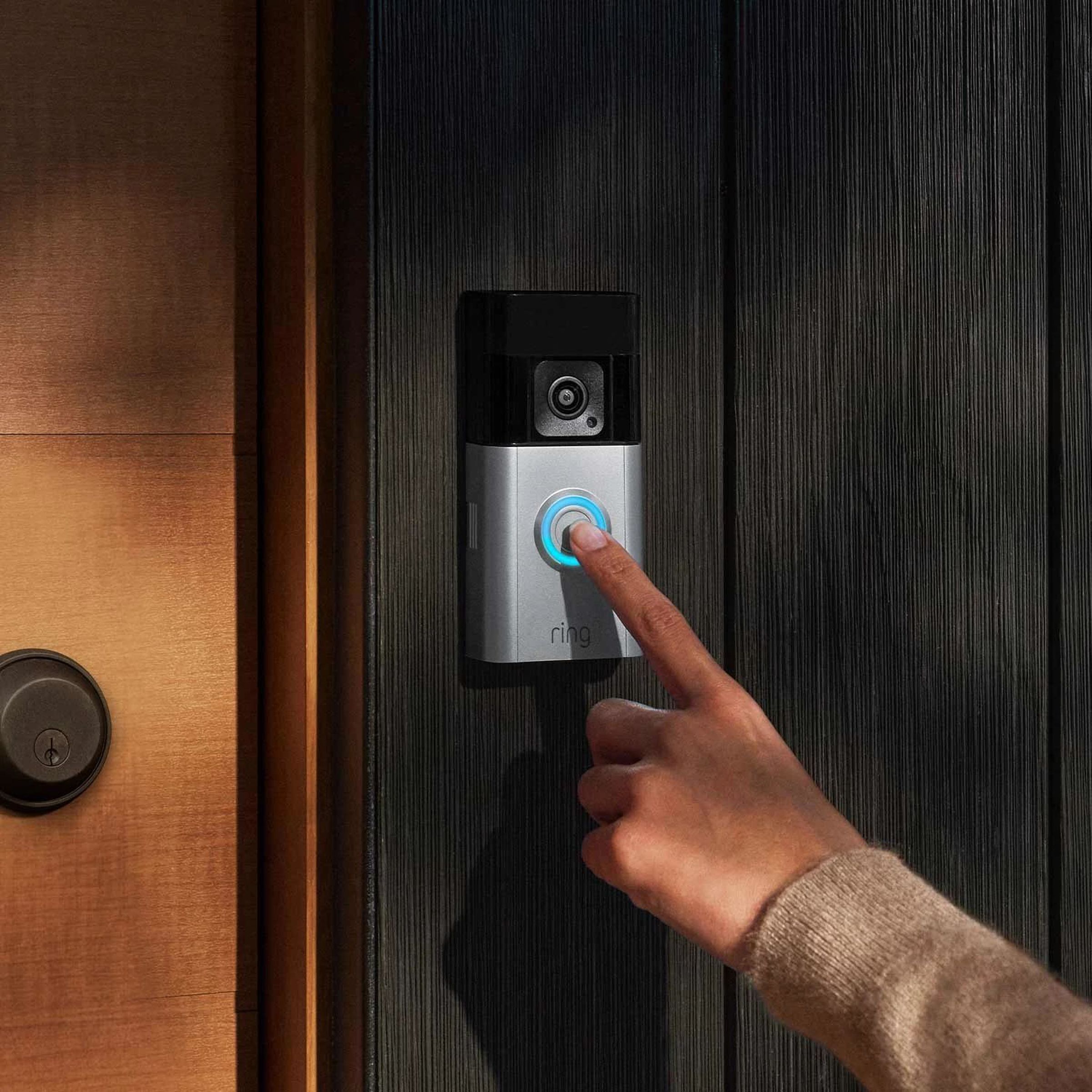 A finger pressing a video doorbell on a door frame.