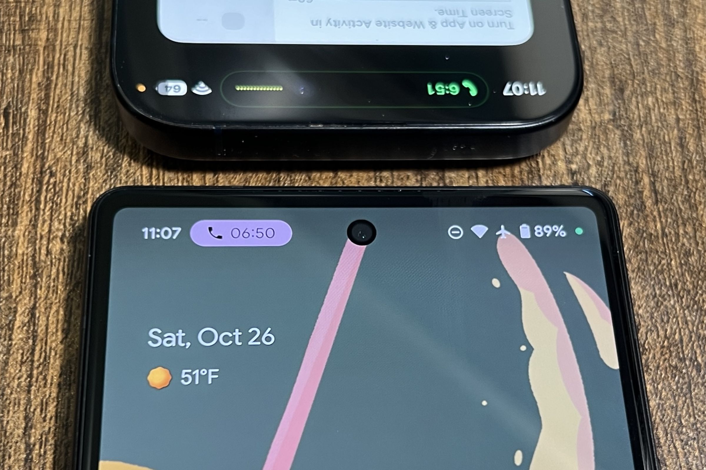 A picture of a Pixel 6 with an ongoing phone call notification, with the top portion of an iPhone 15 Pro screen above it.