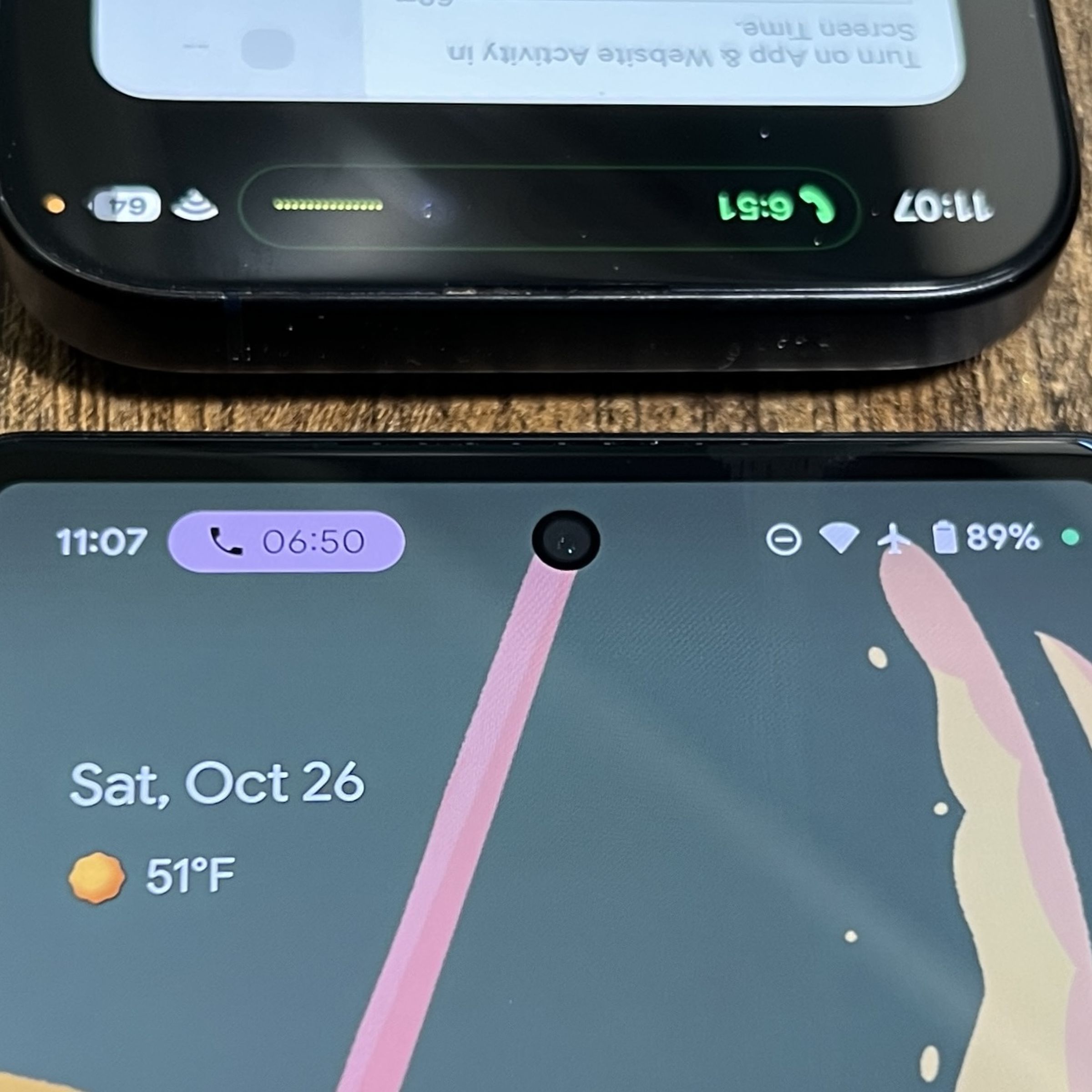 A picture of a Pixel 6 with an ongoing phone call notification, with the top portion of an iPhone 15 Pro screen above it.