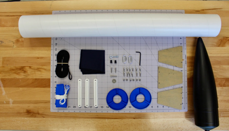 Photo of model rocket components, fins, airframe, motor mount, etc. on a inch-ruled mat for scale