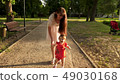 child learns to walk along path in park in summer, mother walks with the baby 49030168