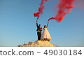 Happy bride and groom waving colored pink smoke against blue sky and laughing. Honeymoon. Romance 49030184