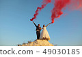 Happy bride and groom waving colored pink smoke against blue sky and laughing. Honeymoon. Romance 49030185