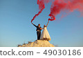 Happy bride and groom waving colored pink smoke against blue sky and laughing. Honeymoon. Romance 49030186