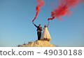 Happy bride and groom waving colored pink smoke against blue sky and laughing. Honeymoon. Romance 49030188