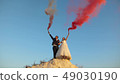 Happy bride and groom waving colored pink smoke against blue sky and laughing. Honeymoon. Romance 49030190