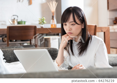 Young woman thinking in front of personal computer in living room 64276219