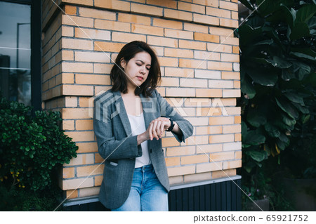 Annoyed female standing by brick wall and checking time 65921752