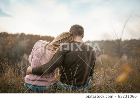 Rear View of hugging tourists sitting on the cliff edge inhaling the aromas of autumn nature outdoors 65231060