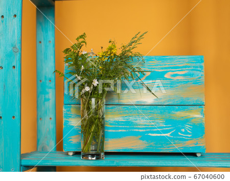 A bunch of summer meadow herbs and flowers in a green glass vase on warm orange yellow and cyan blue wooden plank background. For cards, posters, website decoration etc 67040600