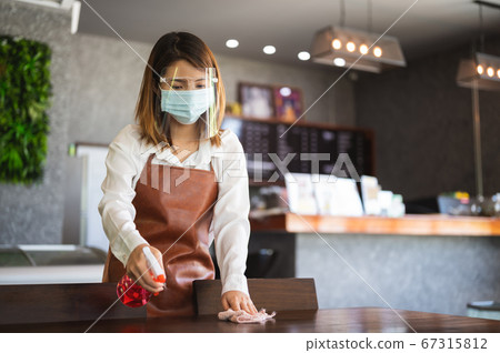 Portrait of female barista wearing mask cleaning table after use  67315812