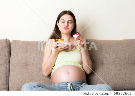 Happy hungry woman enjoys eating delicious cakes relaxing at home. Tasty sweet food during pregnancy concept 69852661