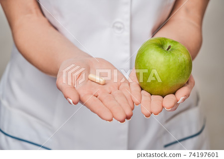 nutritionist doctor healthy lifestyle concept - holding organic fresh green apple and vitamin capsules 74197601