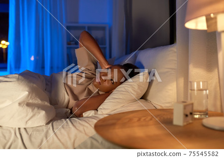 angry african woman lying in bed and closing ears 75545582